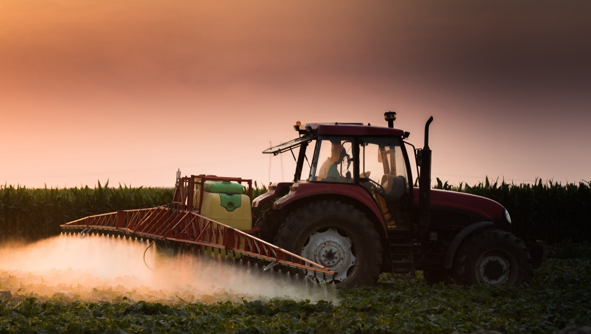 A tractor sprays Paraquat on a field of crops