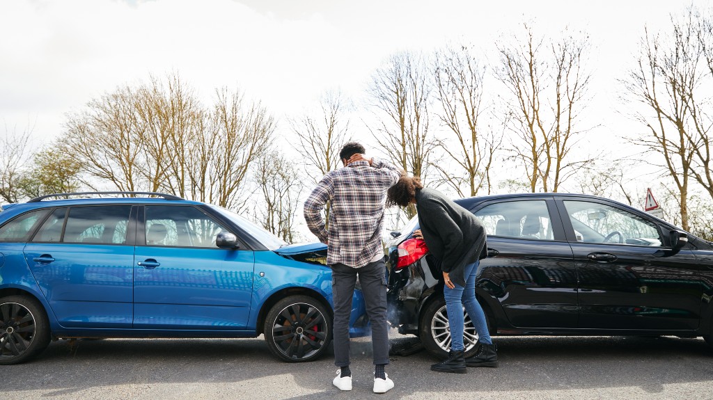 Young male and female drivers looking at damaged car