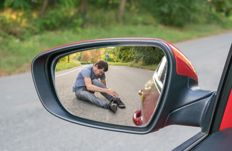 View on injured man on road in rear mirror of a car