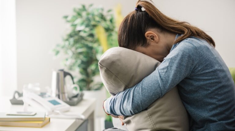 sad woman sitting on the couch hiding her face in the pillow