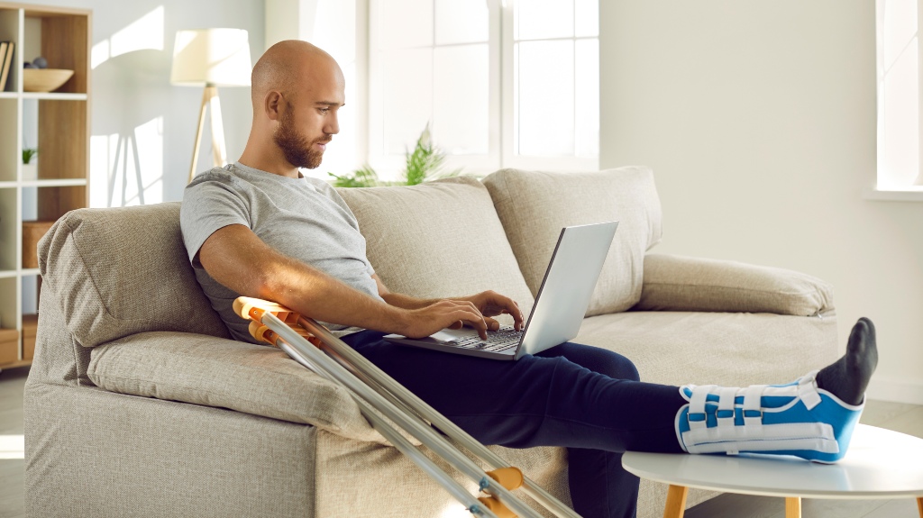 man with injured leg in bandage sit on sofa at home
