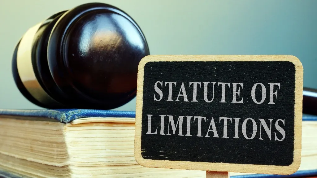 Wooden judge's gavel resting on a book beside a small sign reading "STATUTE OF LIMITATIONS.
