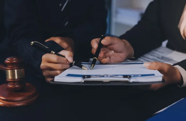Two individuals in formal attire reviewing and signing documents near a wooden judge's gavel.