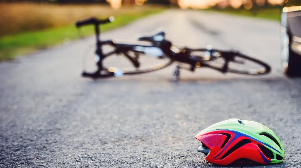 Colorful bicycle helmet on pavement with a fallen black bicycle and a car nearby.