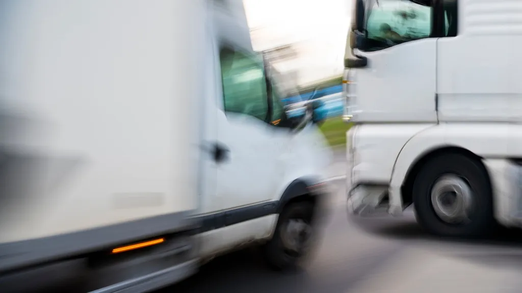Blurred image of two white commercial trucks in motion on a road.