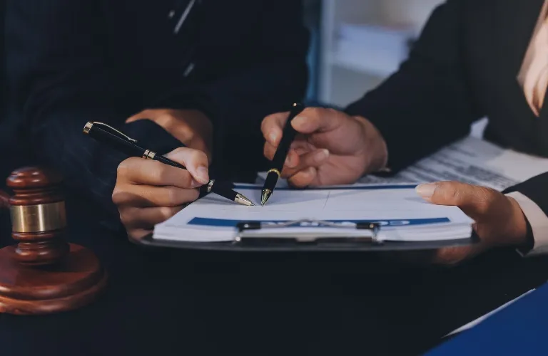 Two individuals in formal attire reviewing and signing documents on a clipboard, with a wooden gavel nearby.