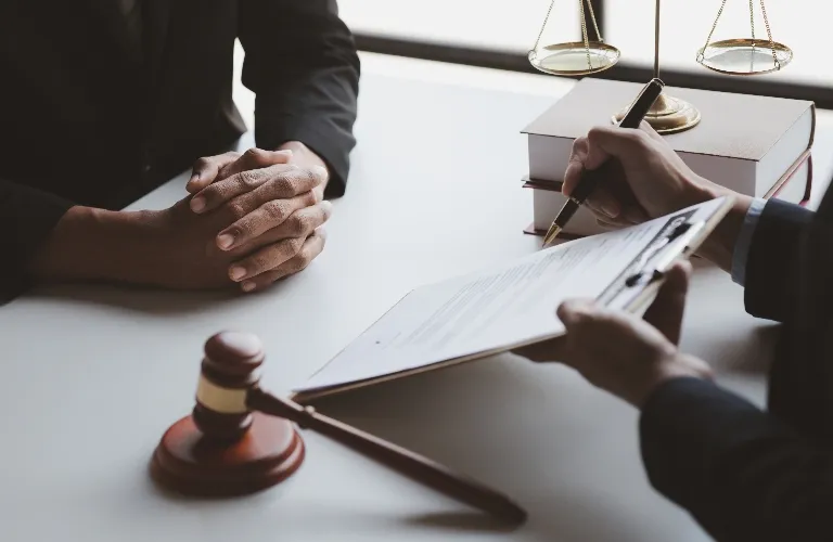 Two individuals in formal attire at a desk with legal books, a gavel, and scales of justice.