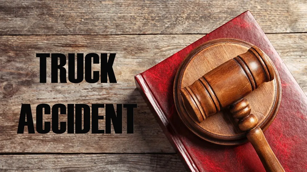 Wooden judge’s gavel resting on a red book beside bold black text reading "TRUCK ACCIDENT" on wooden surface.
