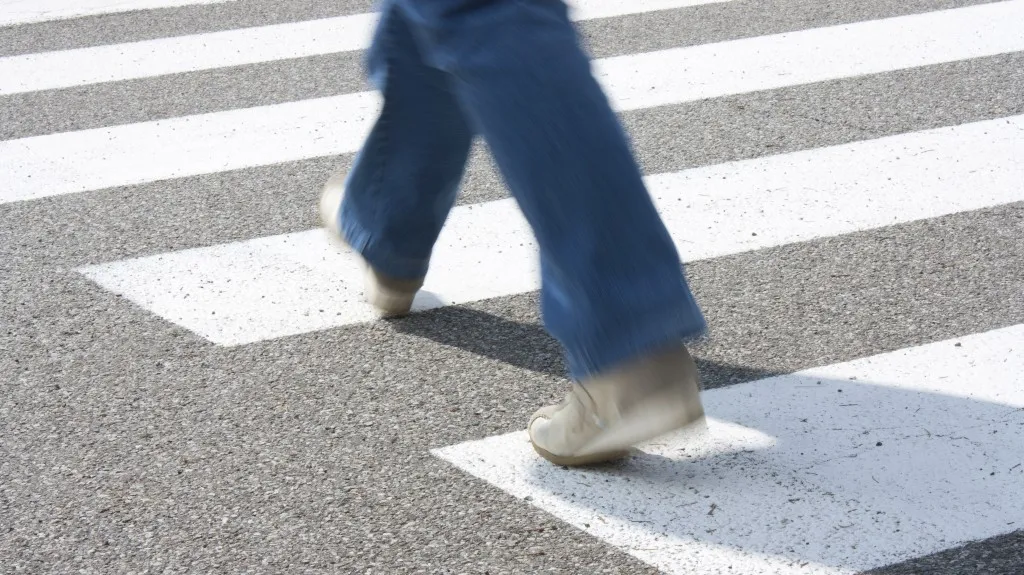 Person wearing blue jeans and white shoes walking across a white-striped pedestrian crosswalk.
