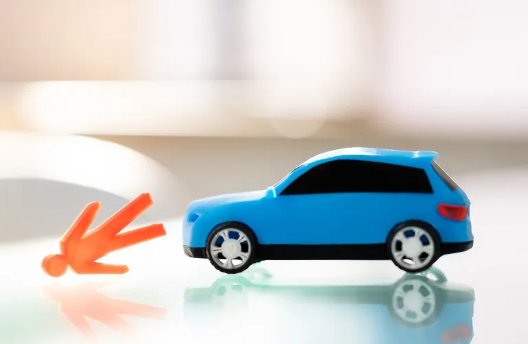 Small blue toy car next to an orange toy figure lying on a reflective surface.