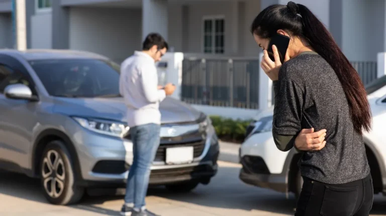 Two individuals near a silver and white car, one woman on phone, one man checking his device.