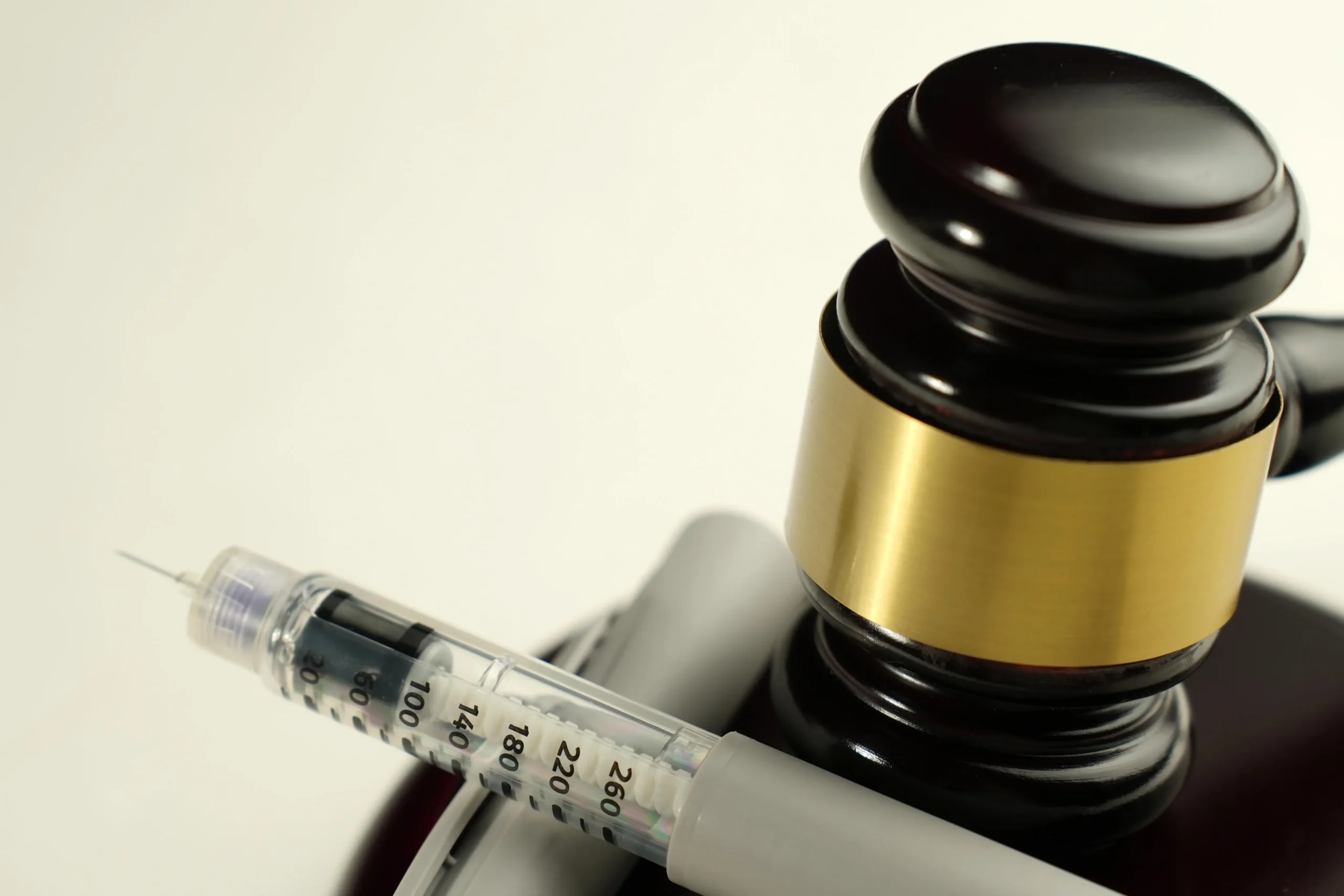 Close-up of a dark wooden judge's gavel with a gold band and a medical syringe on a white background.