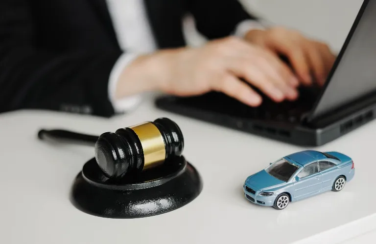 Black and gold judge's gavel and blue toy car on desk with person typing on laptop.